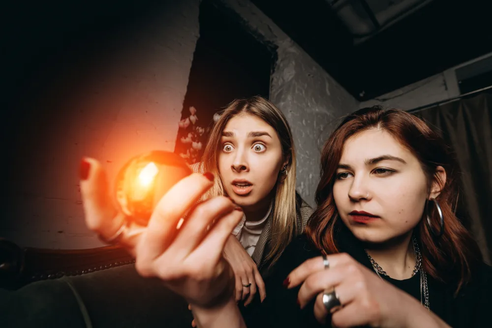Dve prekvapené ženy fascinovane sledovateľné žariacu magickú guľu v rukách počas záhadnej quest hry.